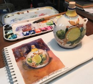 Photograph of vase with a watercolor painting of the same vase on art paper, watercolor palette and brush in the background